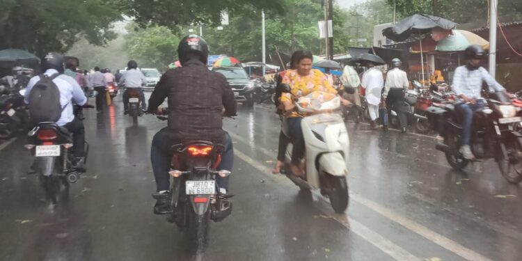 धनबाद के हीरापुर कोर्ट मोड़ पर मंगलवार की दोपहर बारिश में गुजरते राहगीर