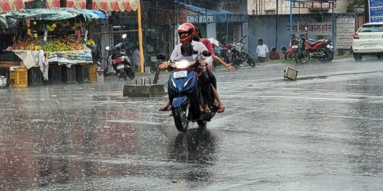 धनबाद की सडक पर बारिश में भीगते बाइक सवार